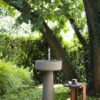 Bjhon 1 Waschbecken von Agape, Design Angelo Mangiarotti. Graues Standwaschbecken in einer grünen Gartenumgebung. Verfügbar in massivem Block Marmor oder hochwertigem Cristalplant®.