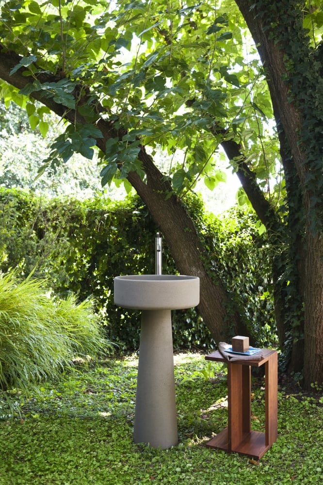 Bjhon 1 Waschbecken von Agape, Design Angelo Mangiarotti. Graues Standwaschbecken in einer grünen Gartenumgebung. Verfügbar in massivem Block Marmor oder hochwertigem Cristalplant®.