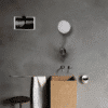 Agape Cube Waschbecken von Benedini Associati im Badezimmer-Konzept mit Wandarmatur, Spiegel und Zubehör an grauer Wand.