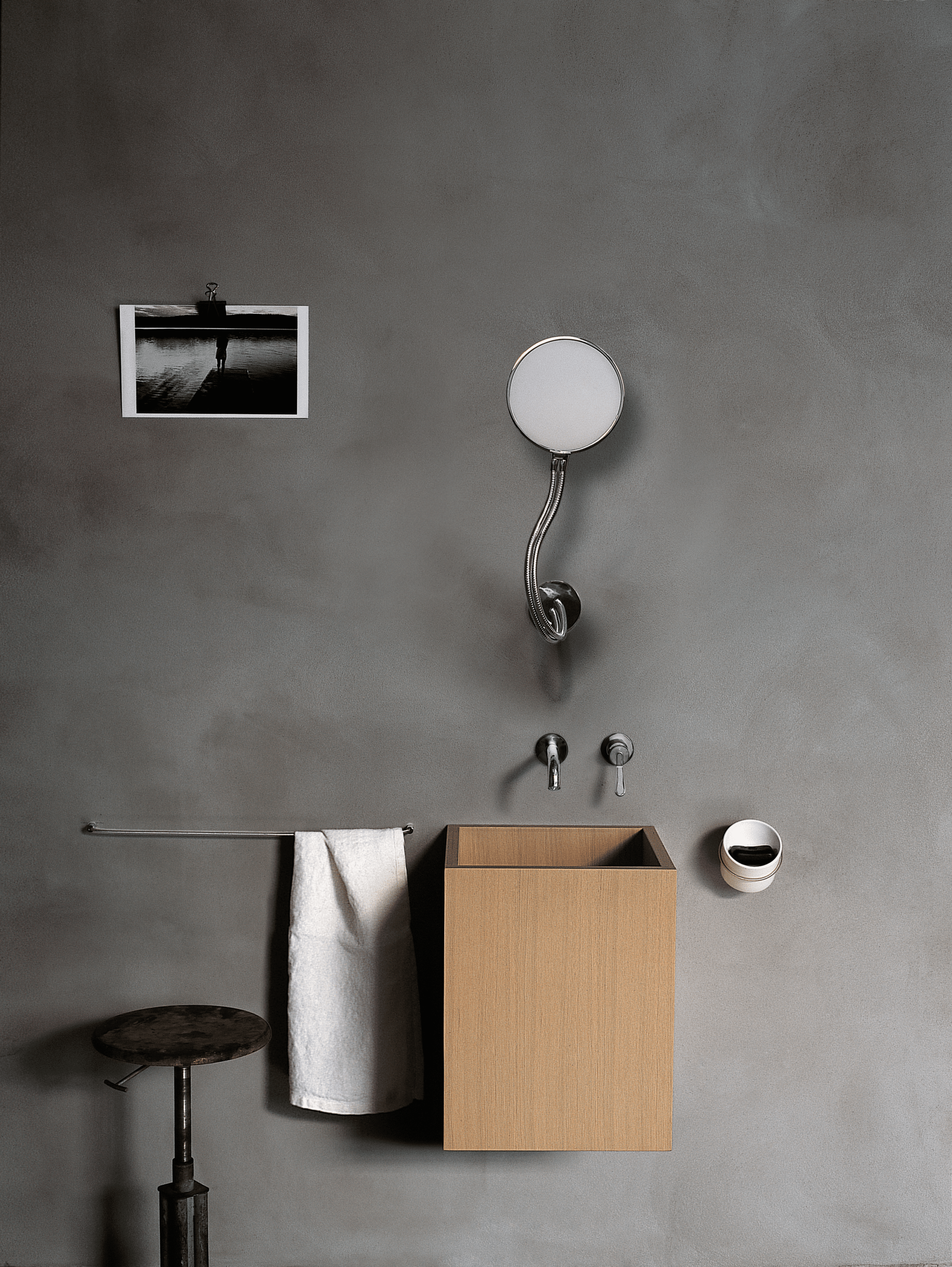 Agape Cube Waschbecken von Benedini Associati im Badezimmer-Konzept mit Wandarmatur, Spiegel und Zubehör an grauer Wand.