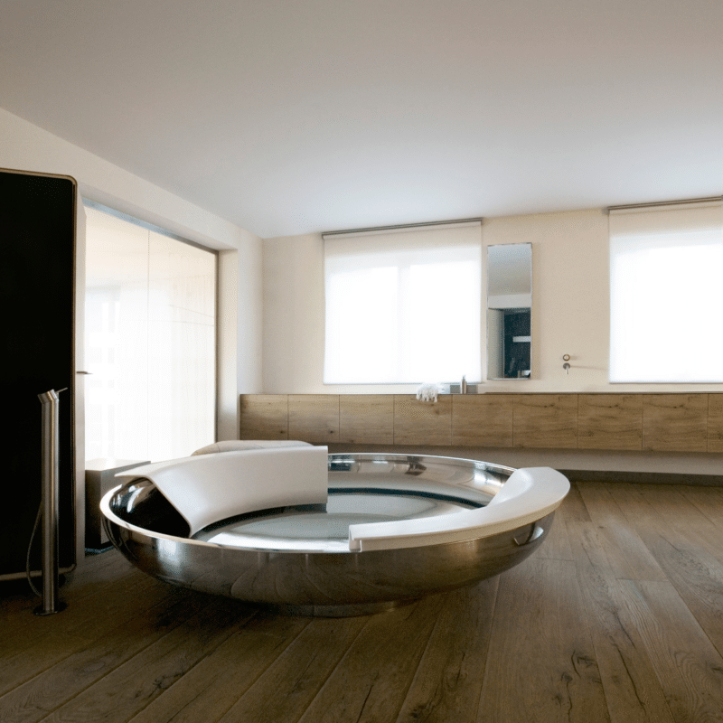 Freistehende runde Badewanne Ufo von Agape aus glänzendem Edelstahl mit weißer Cristalplant Rückstütze, Design Benedini Associati, in einem luxuriösen Badezimmer mit Holzfußboden.