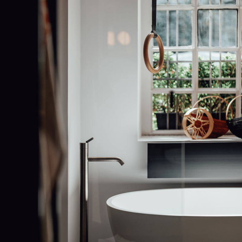 Freistehende Badewanne Spoon M von Agape in reinem Weiß aus Cristalplant biobased Mineralguss, Design Benedini Associati, in einem Badezimmer mit Fenster und bodenstehender Armatur in glänzendem Metall.