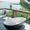 Freistehende Badewanne Spoon M von Agape in dunklem Grau und Weiß, zweifarbig, aus Cristalplant biobased Mineralguss, Design Benedini Associati, platziert auf einem Balkon mit Blick auf ein Gewässer.